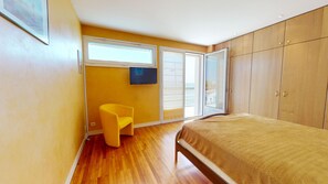 A bedroom with a bed, a chair, a wardrobe, and a window.