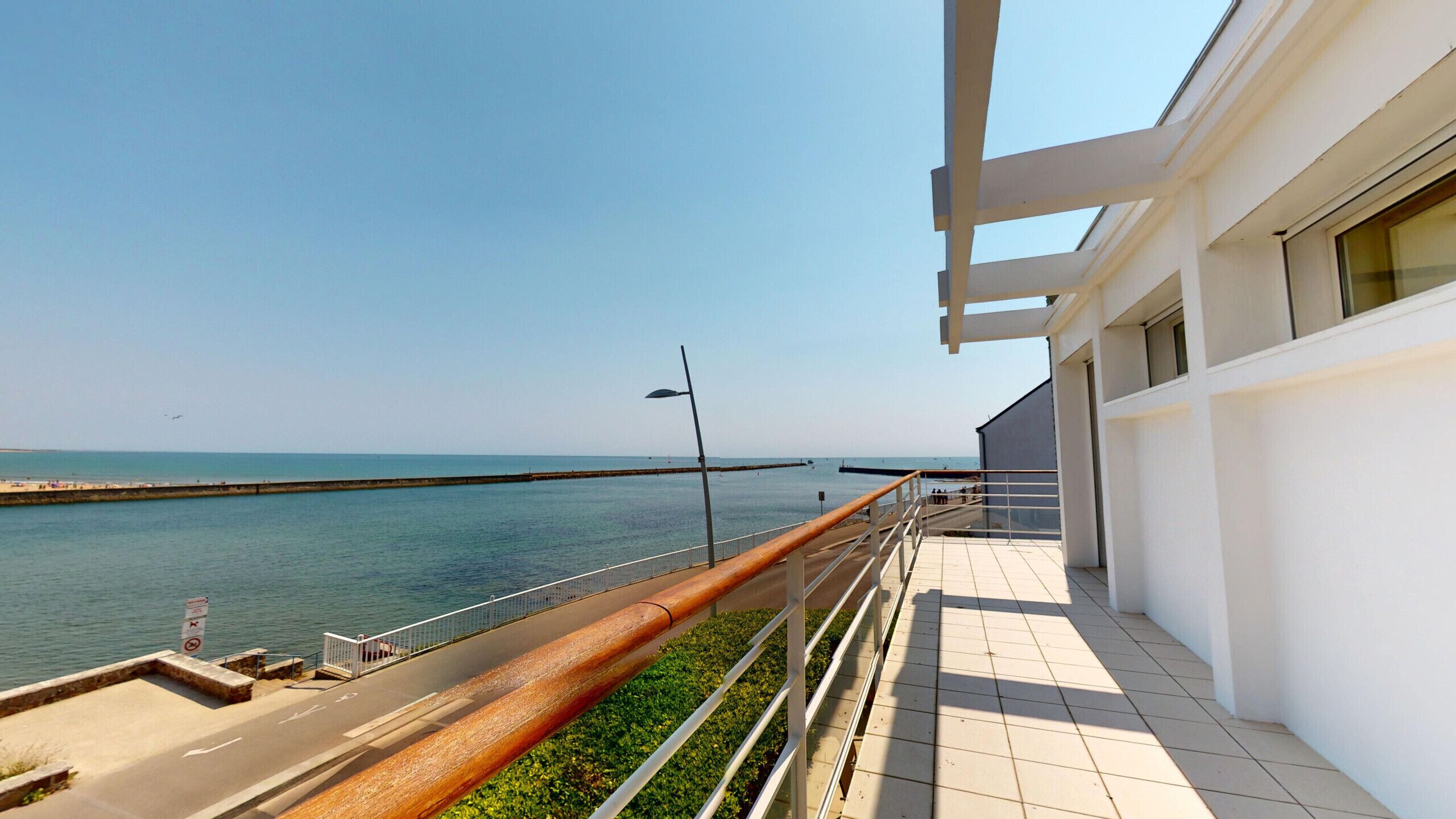 A balcony with a view of the sea and a distant pier.