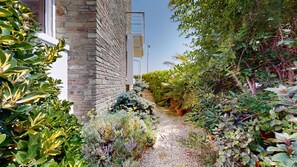 A garden path leading to a stone building with a white door and a window.