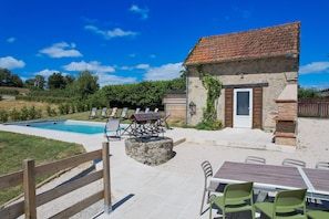 Un bĂątiment en pierre avec un toit en tuiles, une piscine, un espace extĂ©rieur amĂ©nagĂ© pour sâasseoir et une zone dĂ©limitĂ©e par une clĂŽture.