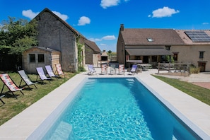 Une piscine avec des chaises longues, un bĂątiment en pierre et une maison avec un toit en tuiles.