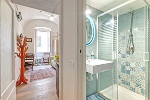 A bathroom with a glass shower enclosure, a white sink, and a patterned tile wall.