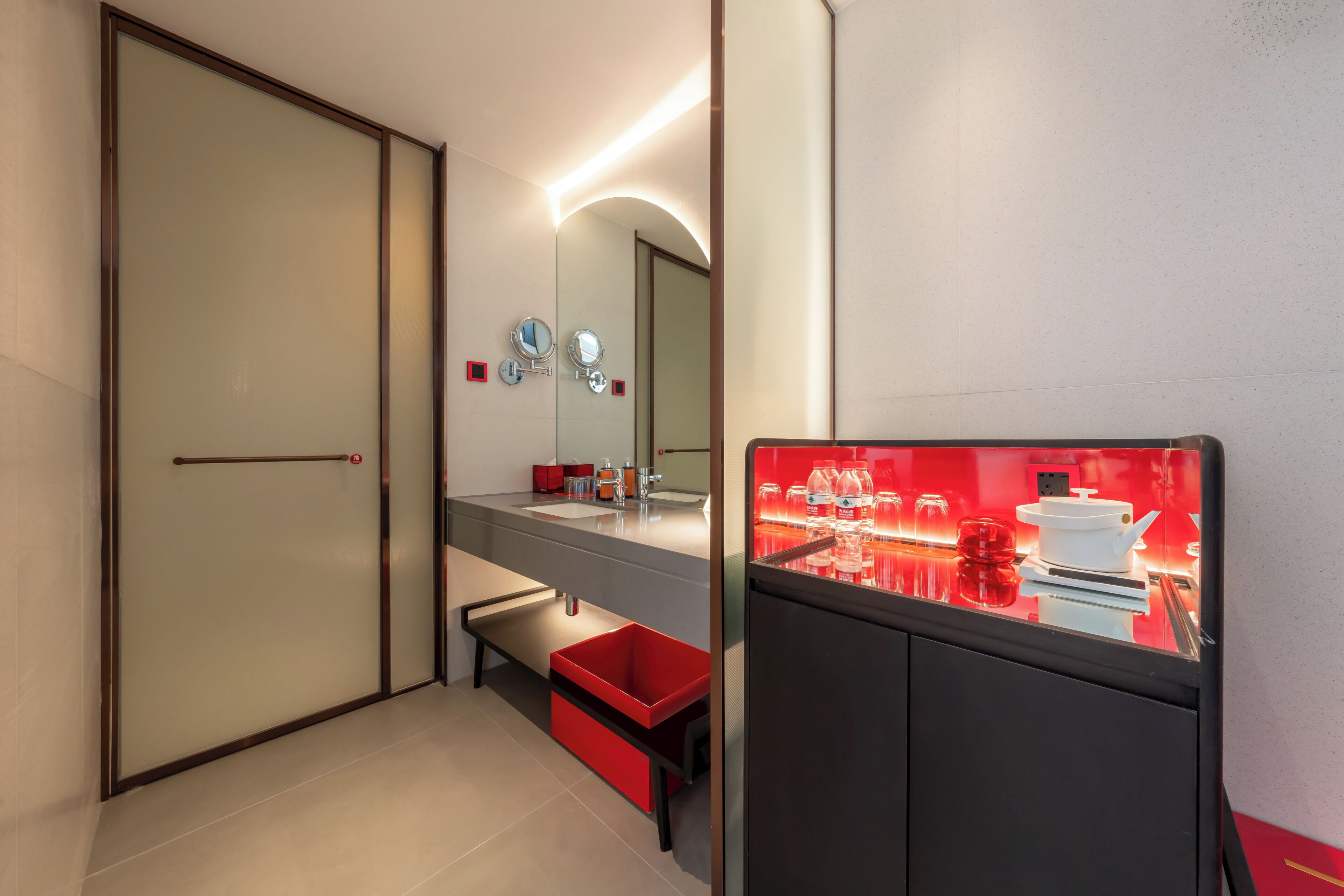 Un baño moderno con un espejo grande, un lavabo rojo y un contenedor de almacenamiento rojo.