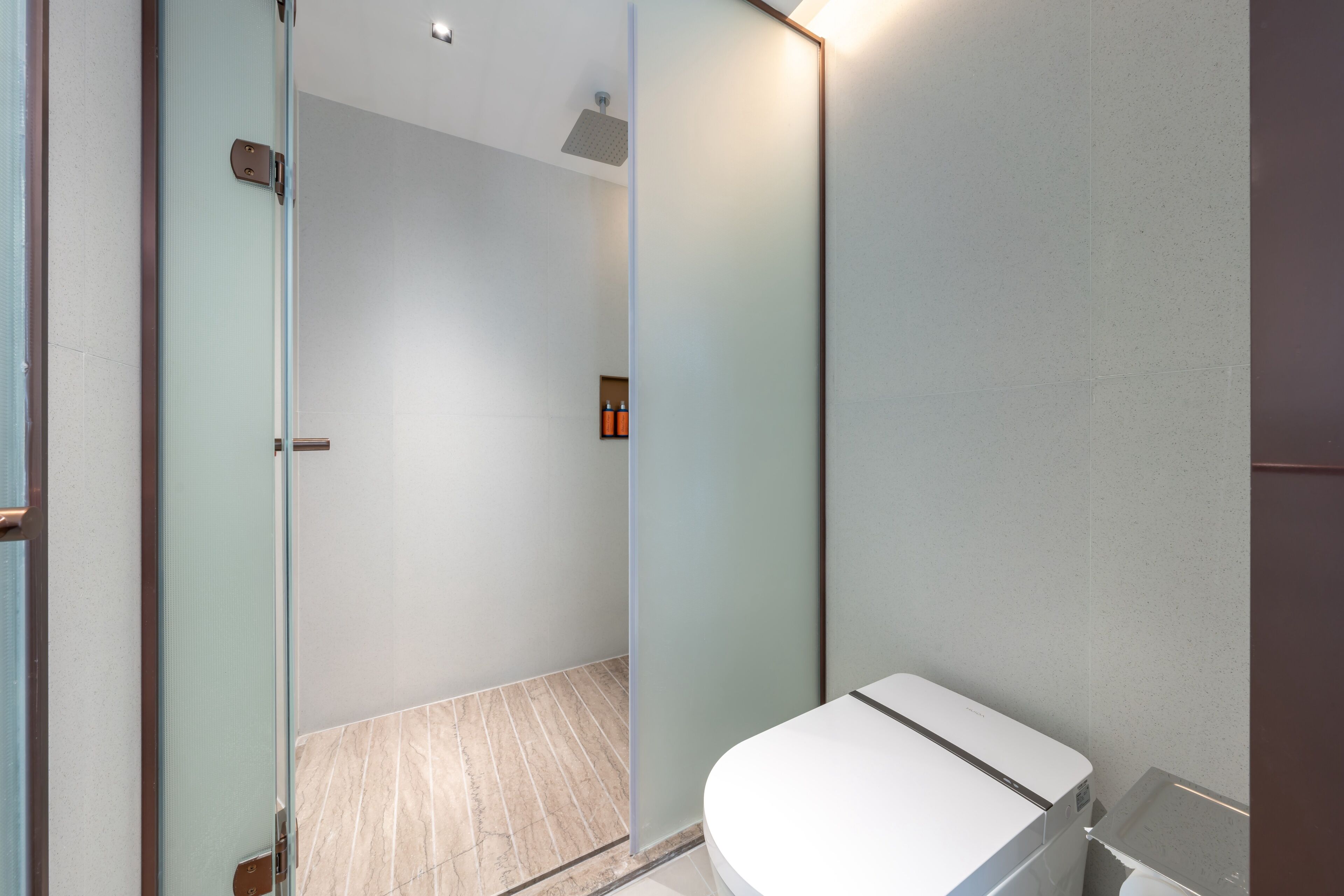 Een moderne badkamer met een douchecabine van glas, een wit toilet en een klein kastje.