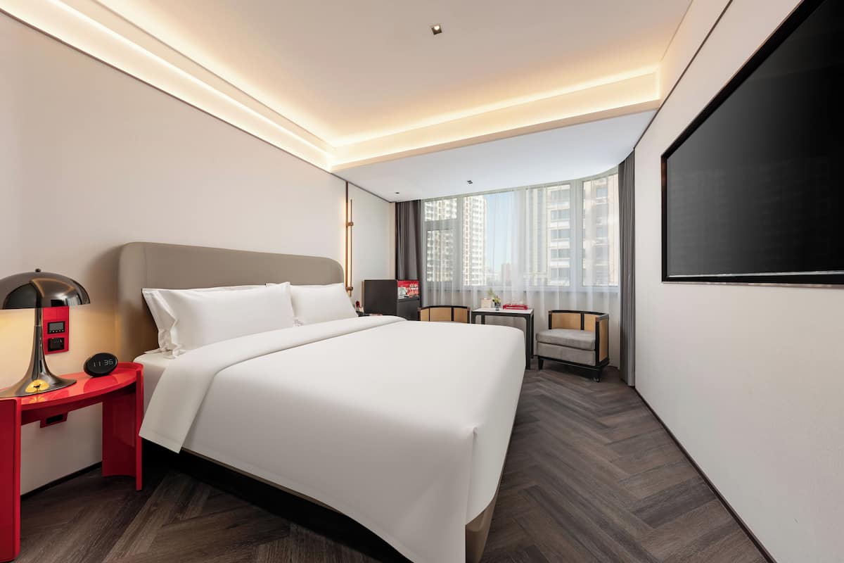 Una habitación de hotel moderna con una cama grande, un escritorio con lámpara, una silla y un televisor.