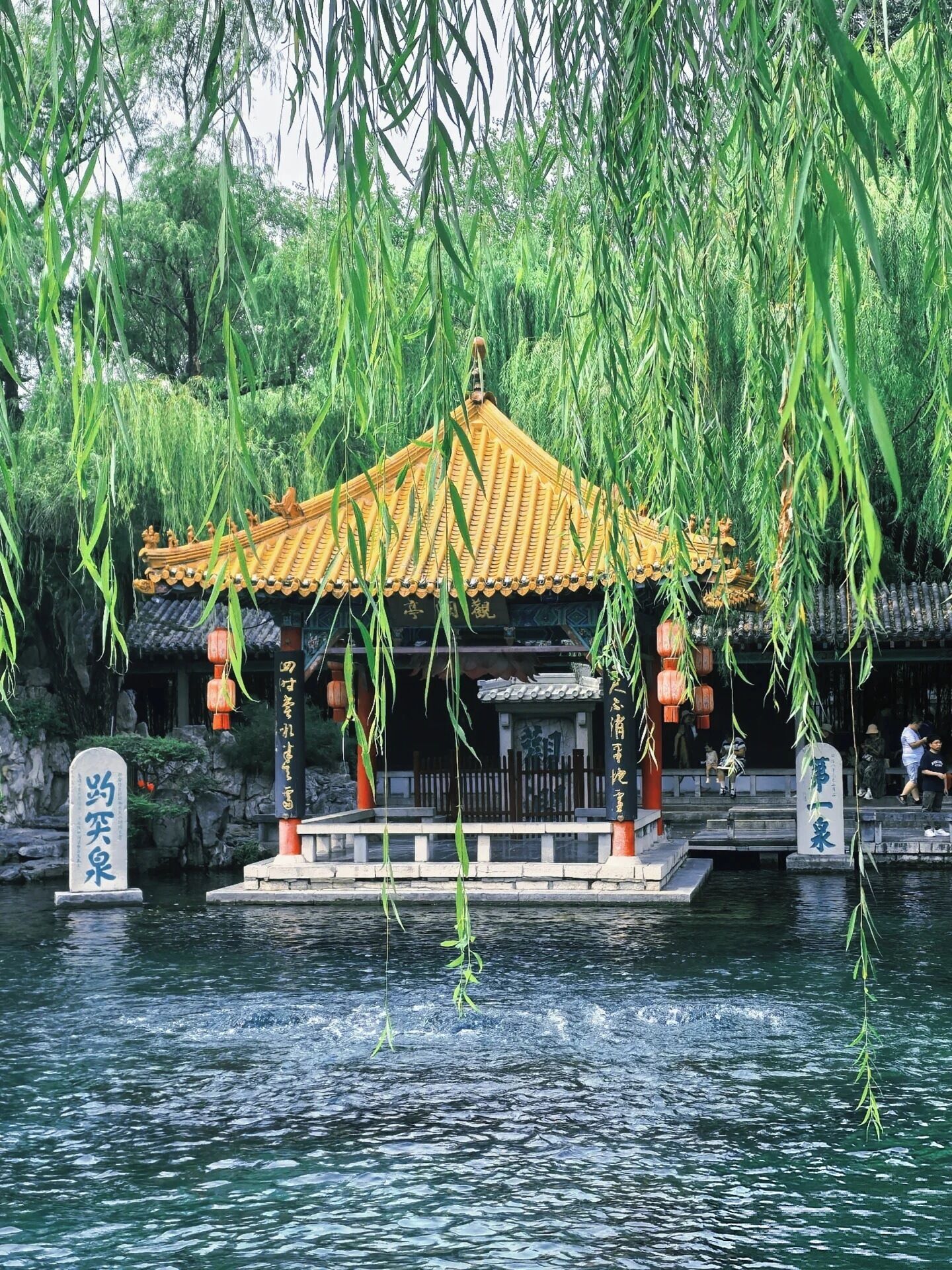 Een traditioneel paviljoen boven het water, met een pannendak, omgeven door groen en stenen constructies.