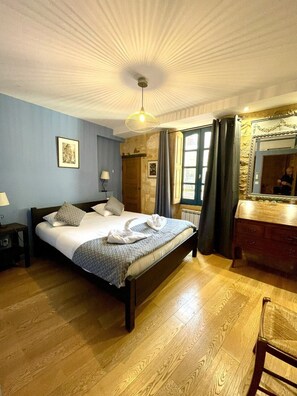 Una habitación de hotel con cama, lámparas de noche, suelo de madera, espejo y ventana con cortinas.