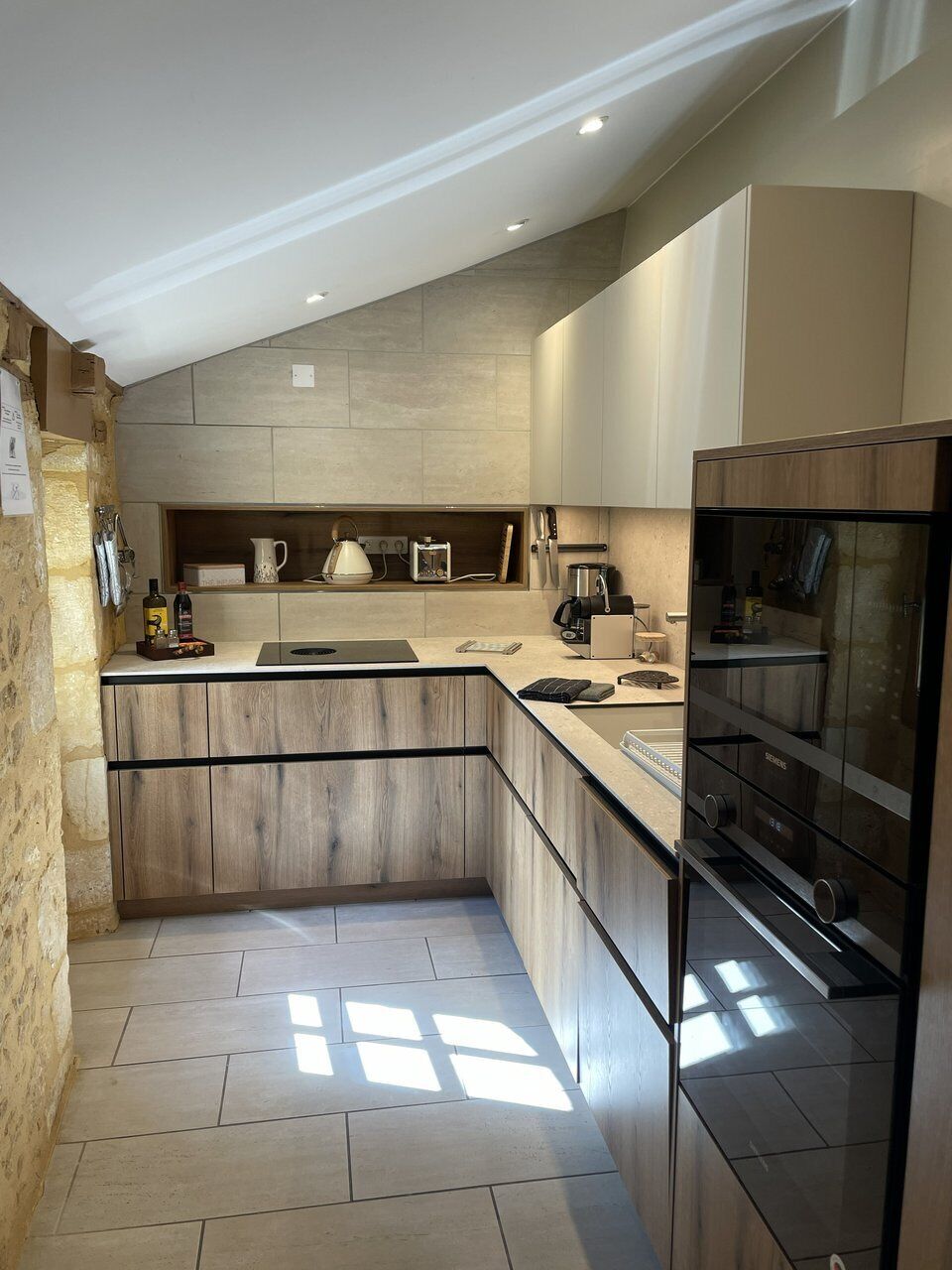 Una cocina moderna con horno empotrado, refrigerador y encimera con varios electrodomésticos.