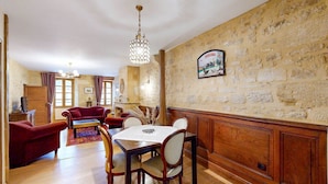 A dining area with a wooden table and chairs, a chandelier, and a stone wall with a sign. - Les Fables - Air-conditioned and downtown (Sarlat-la-Canéda)