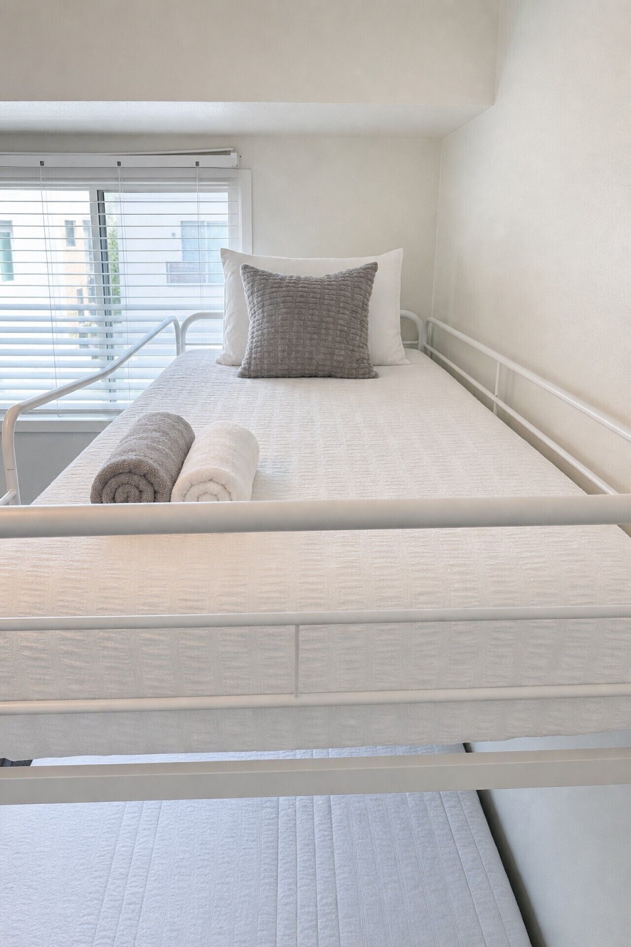 A single bed with a white mattress, a grey pillow, and a rolled grey towel.