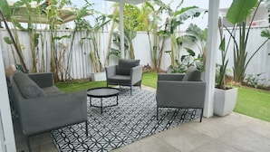 Un patio al aire libre con sofás grises, una mesa redonda y un tapete estampado.