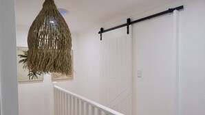 Una escalera con barandilla blanca, una lámpara colgante tejida y una puerta blanca con manija negra.