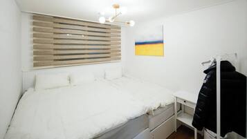 A bedroom with a bed, a desk, a chair, a radiator, a window with blinds, and a painting on the wall.