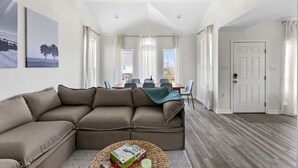 A living room with a sectional sofa, a dining table with chairs, and a door leading to another room. - Palms & Pelicans - recently updated, a block from the beach (Galveston)