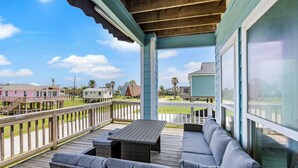 A covered outdoor deck with a seating area, wooden railings, and large windows offering views of the neighborhood. - Palms & Pelicans - recently updated, a block from the beach (Galveston)