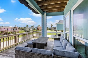 A covered outdoor deck with a seating area, wooden railings, and large windows offering views of the neighborhood.