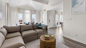 A spacious living room with a sectional sofa, a round wicker coffee table, and a dining area in the background. - Palms & Pelicans - recently updated, a block from the beach (Galveston)