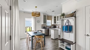 A modern kitchen with white cabinets, a wooden dining table, and a hanging light fixture. - Palms & Pelicans - recently updated, a block from the beach (Galveston)