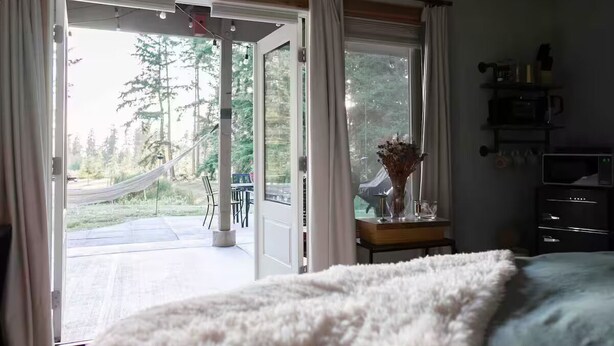 A bedroom with a large bed, a nightstand, a dresser, and a window with curtains.