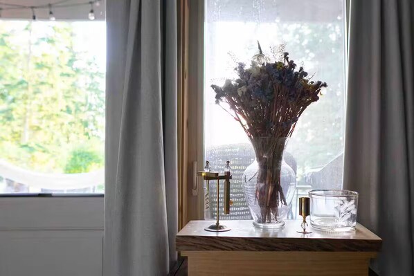 A window with a vase of dried flowers on a wooden table, a candle holder, and a clear glass candle.