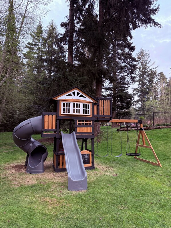 Un parque infantil con tobogán, columpios y una casita de juegos.
