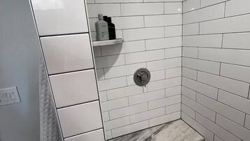 Een douche met witte tegels, een marmeren bankje en een plank met toiletartikelen.