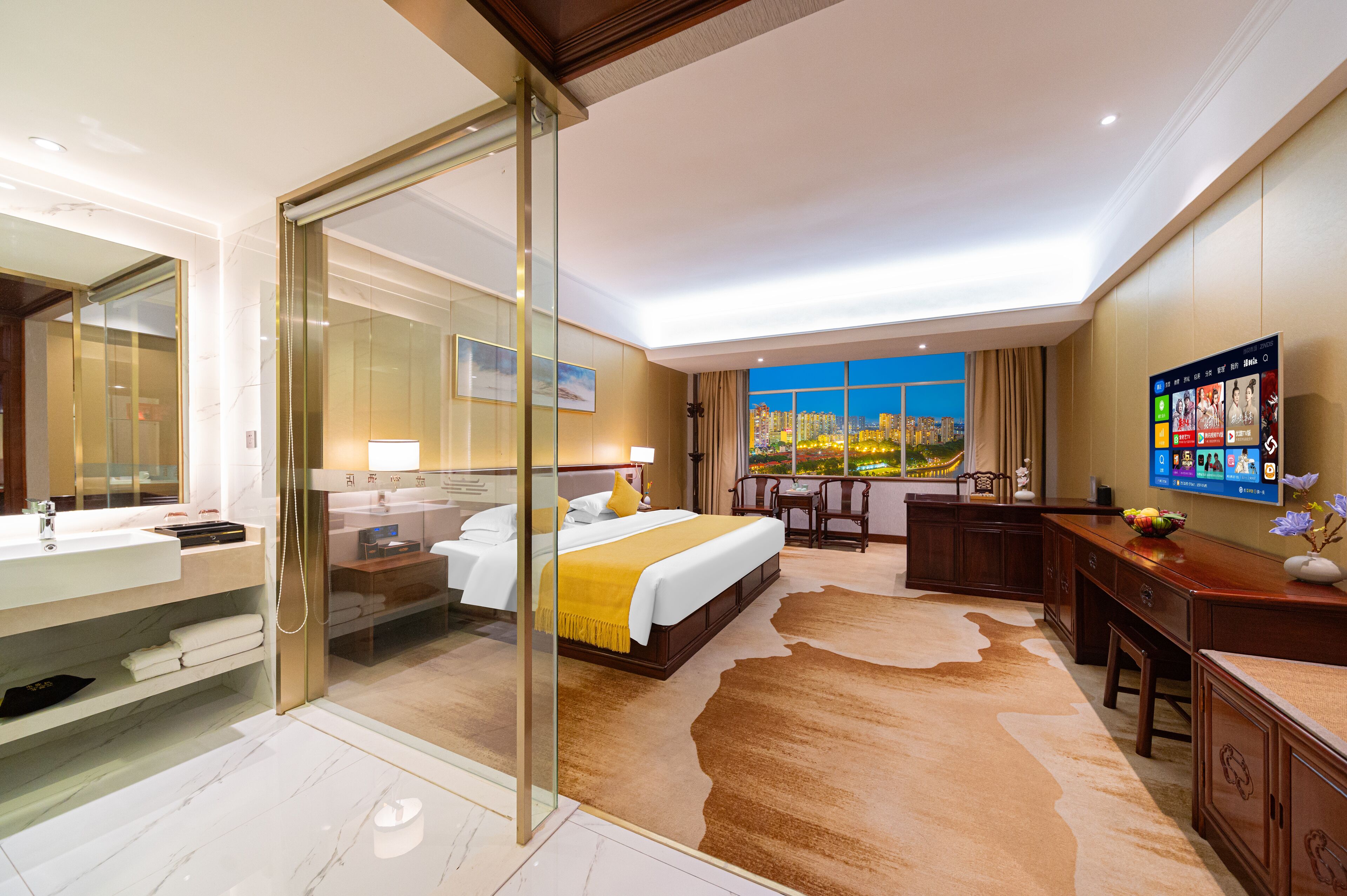 Ein modernes Hotelzimmer mit einem großen Bett, einem verglasten Badezimmer, einem Schreibtisch und Blick auf die Stadt.