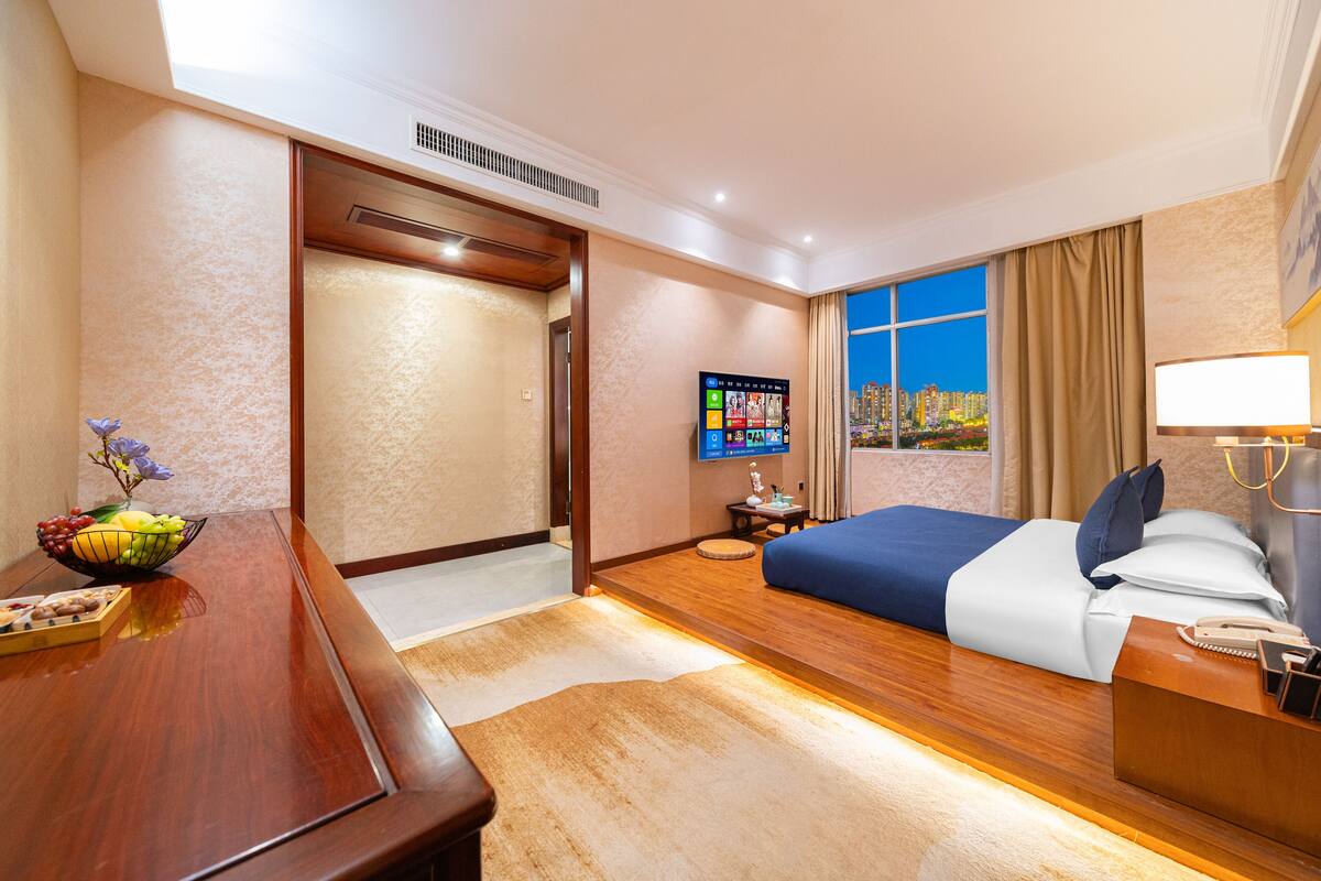Una camera d'albergo con un letto, una scrivania, una TV e una finestra vista città.