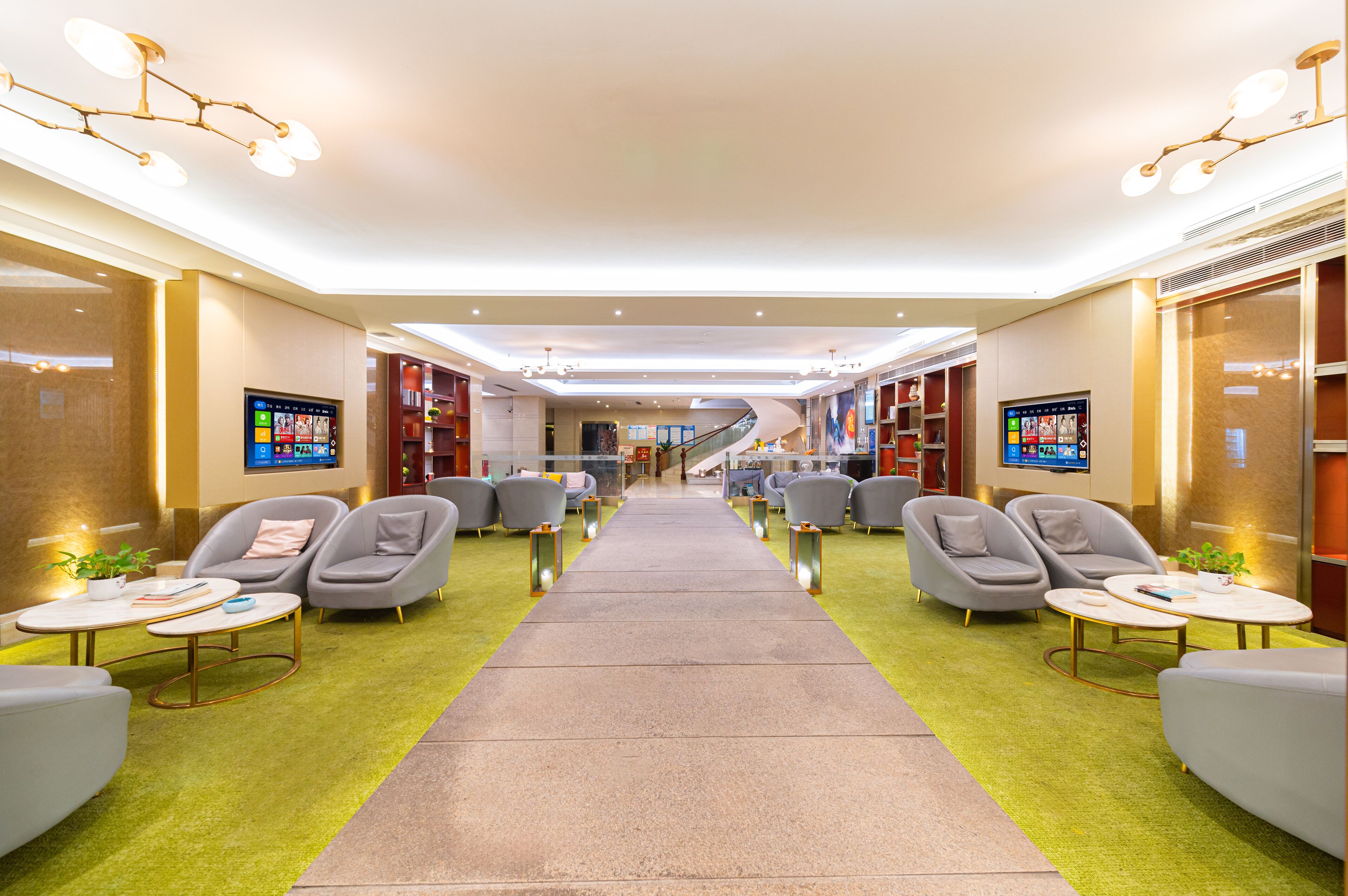 A modern hotel lobby with a central pathway, seating areas, and a staircase leading to upper floors.