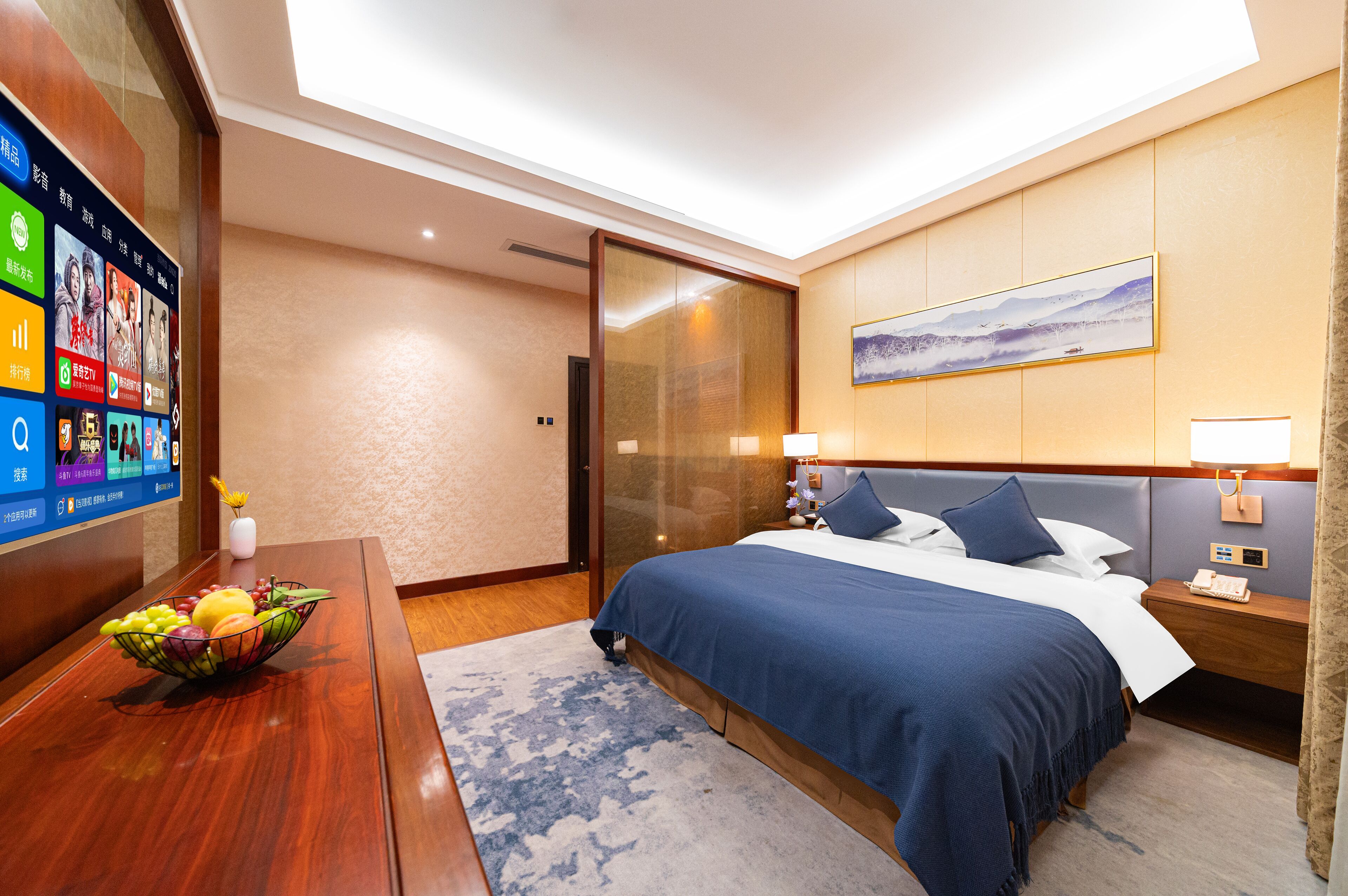 Ett hotellrum med en säng, ett nattduksbord, en lampa och en digital skärm som visar information om hotellets faciliteter och tjänster.