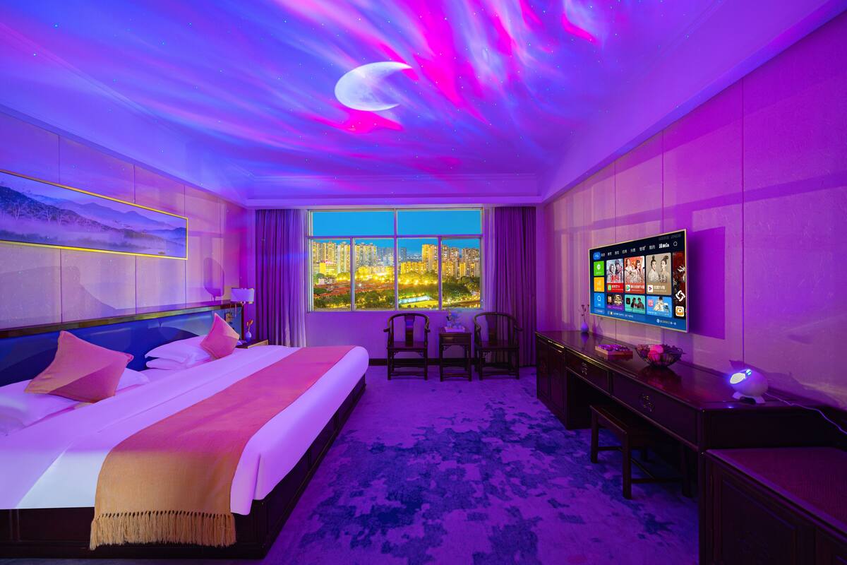 Camera d'albergo con un letto, una scrivania, una TV e vista sulla città attraverso un'ampia finestra.