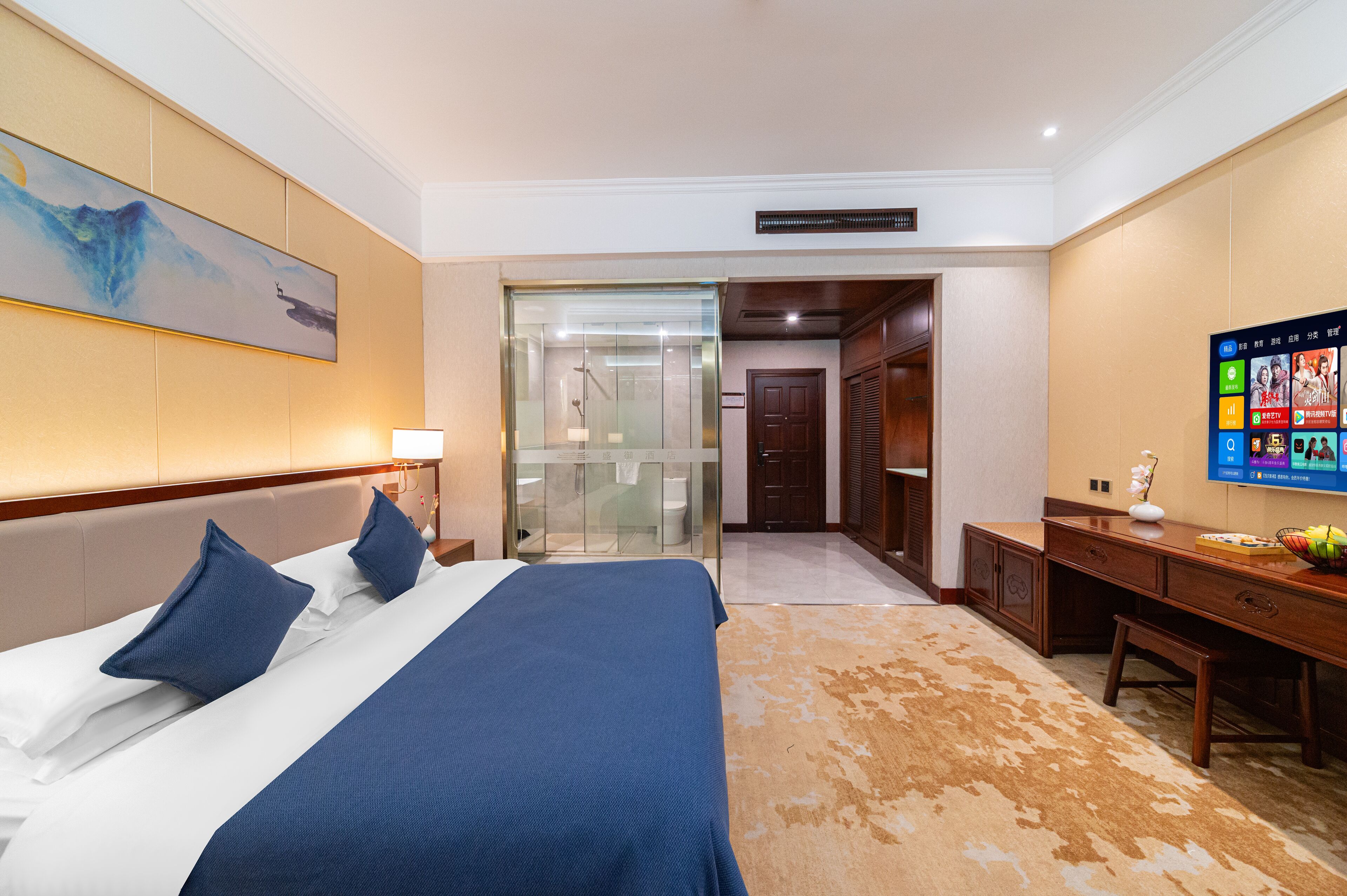 A hotel room with a large bed, a desk, a television, and a bathroom visible through a glass door.