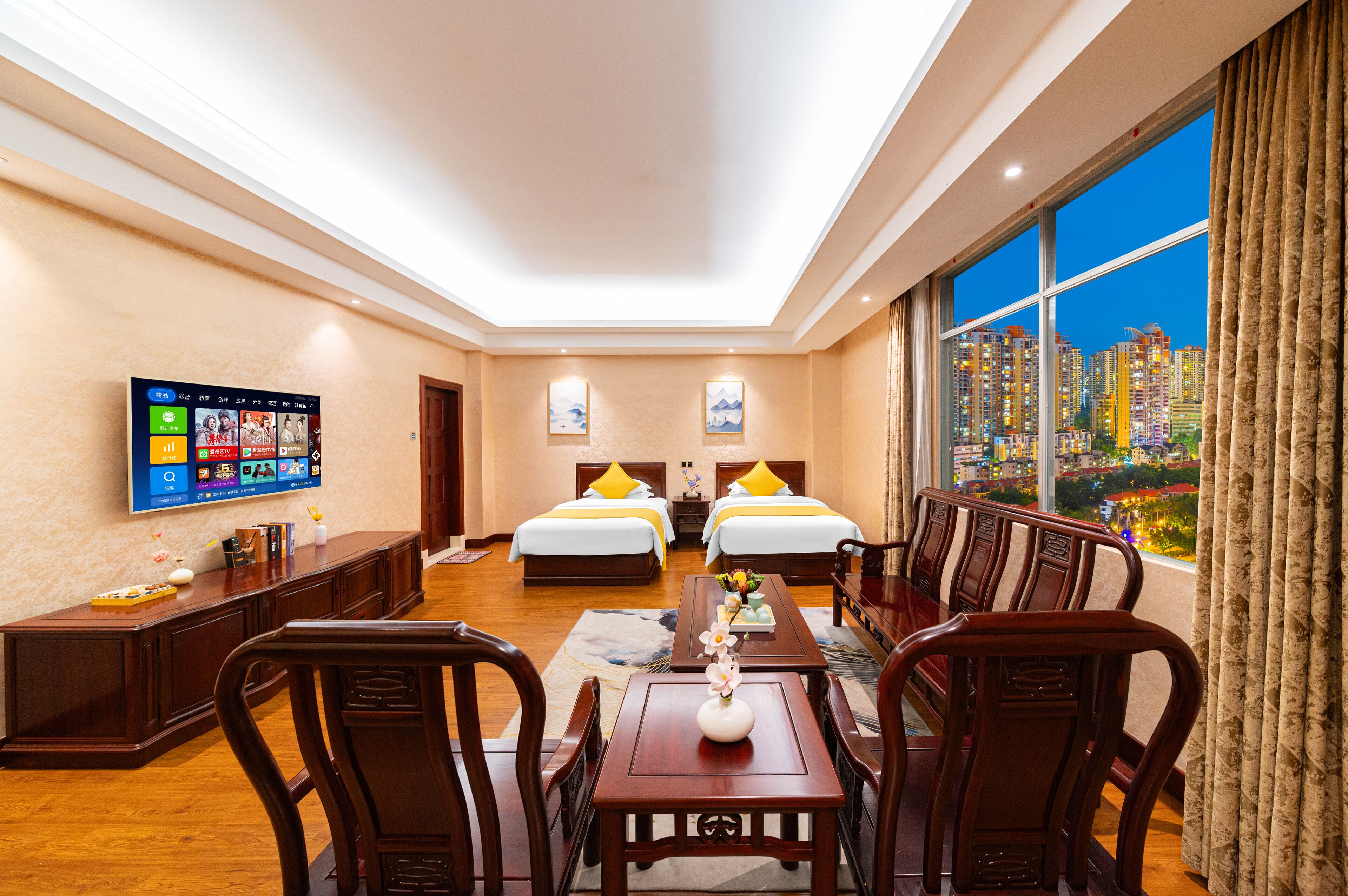 Habitación de hotel con dos camas, una mesa de comedor, sillas, televisión y un ventanal con vistas a la ciudad.