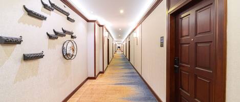 A hotel hallway with a carpeted floor, wooden doors, and wall-mounted light fixtures.