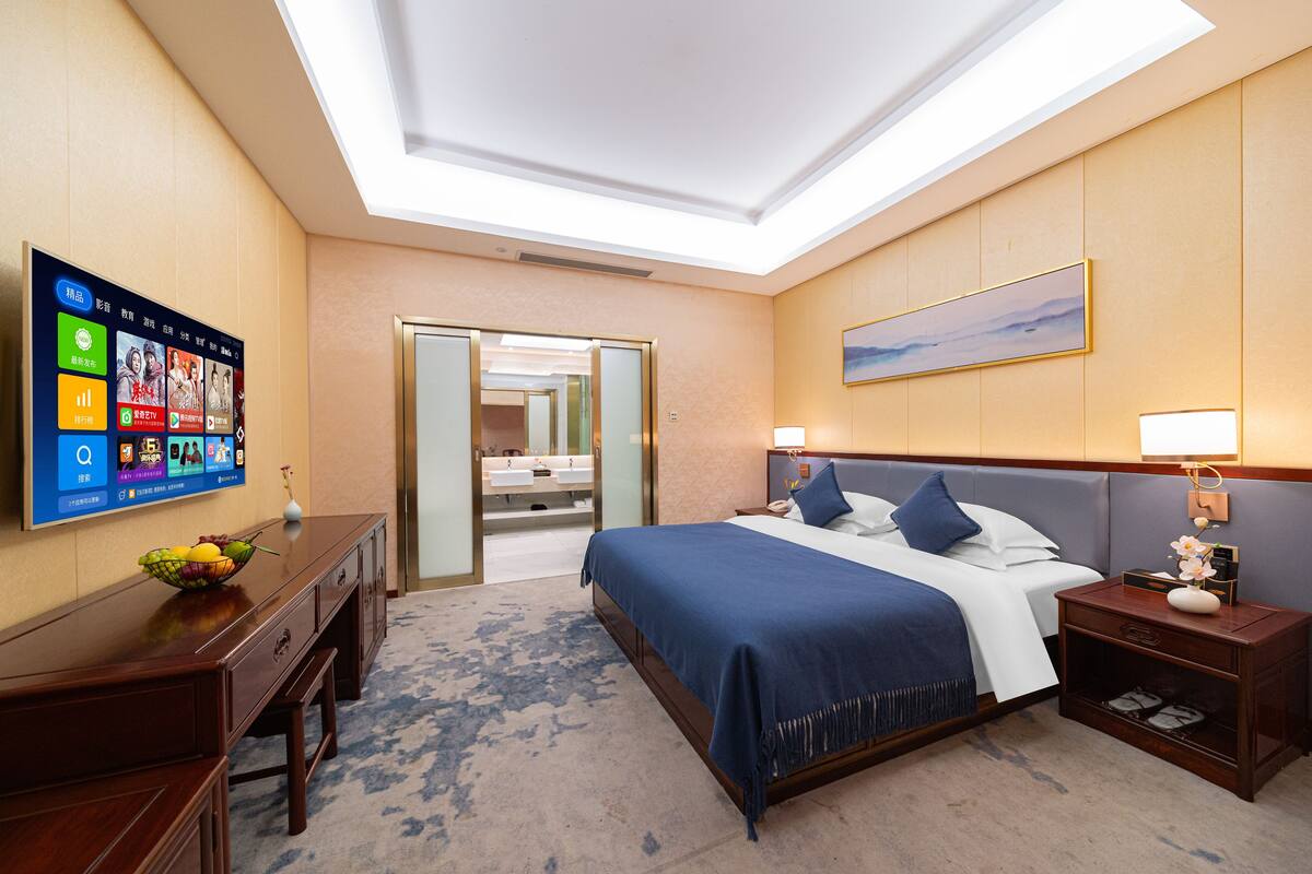 Una camera d'albergo con un letto grande, comodini, una scrivania e un televisore che mostra un menu.