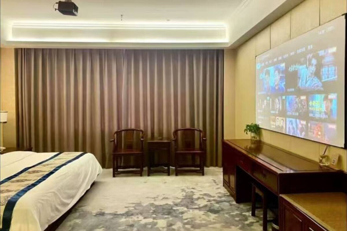 Una camera d'albergo con un letto, una scrivania, una sedia, uno schermo televisivo e un'ampia finestra con tende.
