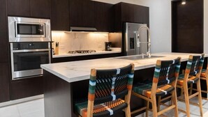 Una cocina moderna con armarios oscuros, electrodomésticos de acero inoxidable y una isla central con taburetes de bar.