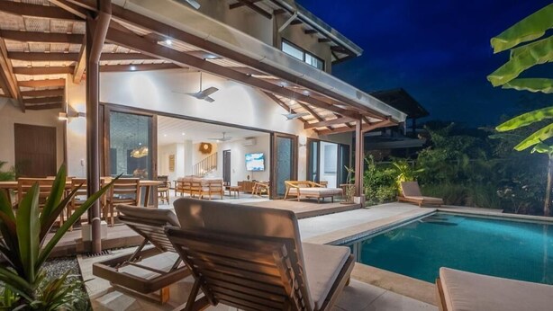 Una casa moderna con piscina, mobiliario exterior y un porche cubierto.