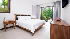 Un dormitorio con una cama, mesitas de noche de madera, un escritorio, un ventilador de techo y vistas a zonas verdes.