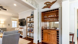 Una sala de estar con sofá, televisión, estantería y un aparador de madera con copas de vino.