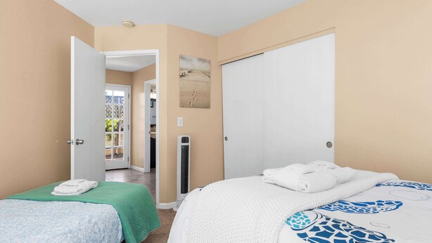 Une chambre d’hôtel avec deux lits, une couverture verte et une couverture blanche, une porte donnant sur un balcon et un tableau accroché au mur.