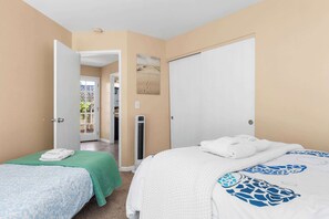 Une chambre d’hôtel avec deux lits, une couverture verte et une couverture blanche, une porte donnant sur un balcon et un tableau accroché au mur.