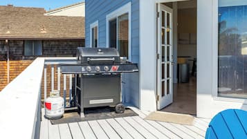 A barbecue grill on a deck with a house in the background.