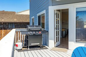 A barbecue grill on a deck with a house in the background.