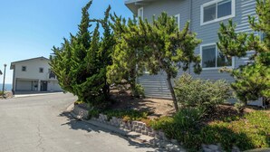 Une maison d’habitation avec un garage, une allée et un jardin bien entretenu, agrémenté de divers arbustes et arbres.