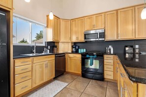 Una cocina moderna con armarios de madera, un microondas de acero inoxidable, un horno negro y una ventana que proporciona luz natural.