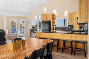 A modern kitchen with wooden cabinets, a black refrigerator, and a dining area with a wooden table and chairs.