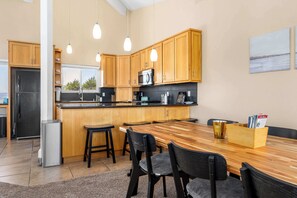A modern kitchen with wooden cabinets, a stainless steel refrigerator, a microwave, and a wooden dining table with chairs. - Sand Dollar Beach Home - Stunning views! (La Selva Beach)