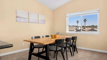 A room with a wooden table, six chairs, and a window with a view of palm trees and houses.