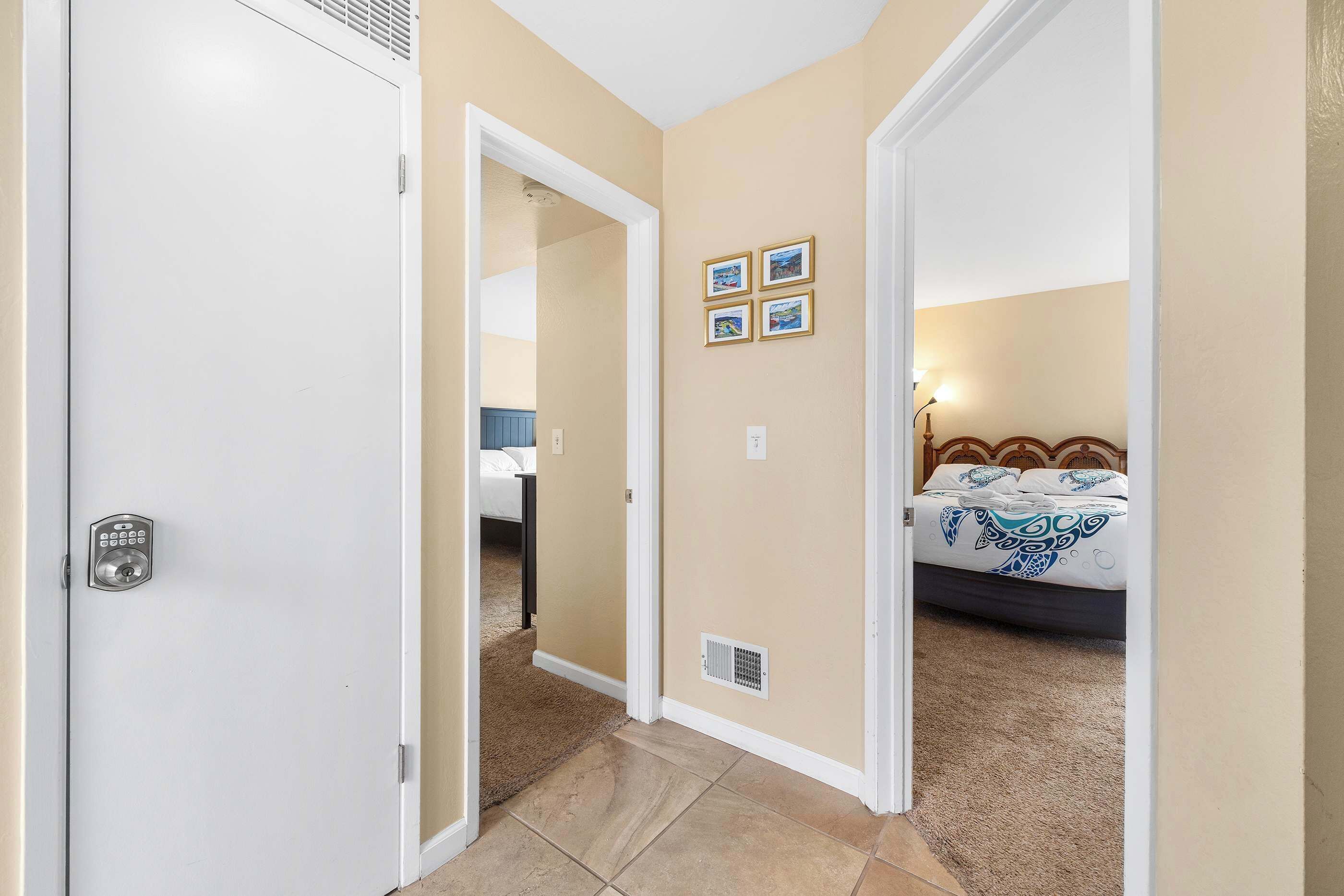 A hotel room with a bed, a bedside table, a lamp, and a door with a keypad lock.